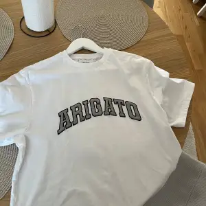 Axel Arigato, Vit T-shirt med grått märke. Något oversized modell. Använd 1 gång, är som nyskick. 