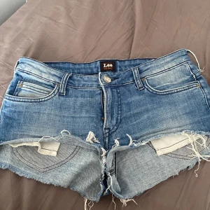 Blå jeansshorts från Lee - Säljer ett par snygga blå jeansshorts från Lee. De har en cool, sliten look med fransiga kanter och klassisk femficksdesign. Perfekta för sommardagar eller festivaler! 🕶️