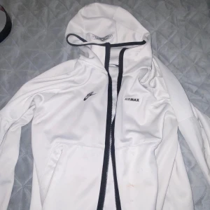 Vit vindjacka från Nike Air Max - Säljer en snygg vit vindjacka/ hoddie från Nike Air Max. Jackan har en dragkedja framtill och en huva med snörning. Perfekt för vår och höst när det blåser lite extra. Den är långärmad och har en stilren design med Nike-loggan på bröstet.