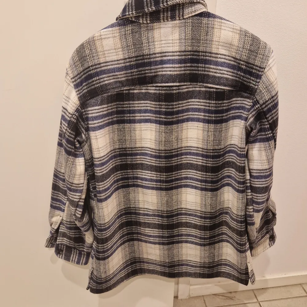 Säljer en snygg och trendig rutig overshirt i blått och vitt. Den har långa ärmar och knappar framtill. Perfekt för höst och vår när du vill ha något stilrent och bekvämt. Passar både till vardags och lite mer uppklädda tillfällen. Stor i storleken.. Jackor.