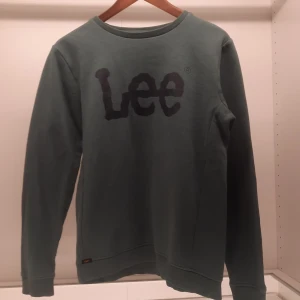Grön sweatshirt från Lee - Säljer en grön sweatshirt från Lee med ett stort tryck av märkesnamnet på framsidan. Tröjan har långa ärmar och en rund halsringning. Perfekt för en avslappnad stil.