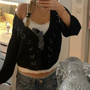 Svart stickad kofta med rosett från hm - Säljer en svart stickad kofta med ett fint mönster och en söt rosett framtill. Koftan har en offshoulder-design och långa ärmar, perfekt för en trendig look. Passar bra till jeans eller kjol för en avslappnad stil.