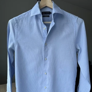 Riley ljusblå skjorta med struktur, storlek S - Riley skjorta mjuk och skön att ha på sig. Mycket fint skick. Slim fit, storlek S. Ljusblå, fin struktur. 100% bomull. Jag säljer många skjortor i samma storlek, kolla gärna på mina övriga annonser för att skapa ett paket. Axelbredd: 42 cm Längd: 72 cm  Kostymskjorta, business, finskjorta, struktur