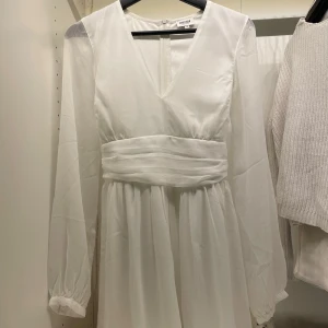 Vit klänning från Bubbleroom - Elegant vit klänning från Bubbleroom med långa ärmar och v-ringad design. Klänningen har en vacker rosett i ryggen och ett brett midjeband som ger en smickrande passform. Perfekt för speciella tillfällen som exempelvis studenten/skolavslutning!! Endast använd en gång och inga defekter🎀pris kan absolut diskuteras!
