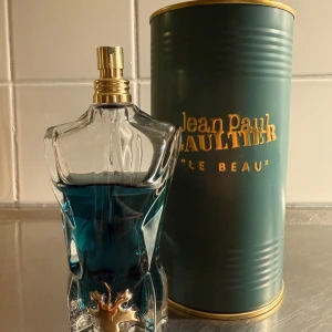 Le Beau Edt från Jean Paul Gaultier - Säljer en Jean Paul Gaultier Le Beau Eau de Toilette i en unik flaska formad som en manlig torso. Parfymen har en djupblå färg och kommer i en elegant grön metallförpackning. Flaskan pryds av en gyllene detalj framtill. Perfekt för den som vill ha en distinkt och stilren doft. Även perfekt nu inför våren och sommaren. Runt 75/80 av 125ml kvar. Nypris 1400kr mitt pris 699kr! Hör gärna av er om ni har några frågor eller bud! 