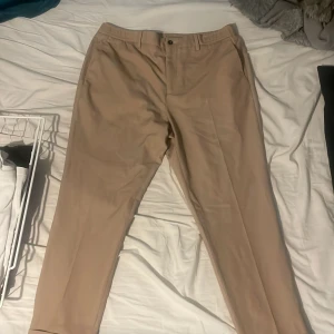 Beige kostymbyxor från Zara - Snygga beige kostymbyxor från Zara i en klassisk stil. Byxorna har en midwaist design och är perfekta för en stilren look. De har en knapp och dragkedja framtill för enkel stängning.