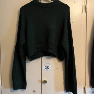 Mörkgrön stickad tröja från Divided - Säljer en snygg mörkgrön stickad tröja från Divided. Tröjan är croppad med långa ärmar och har en ribbad design. Passar bra till jeans eller kjol för en avslappnad look. Köpte på HM för ca 1,5 år sedan men har aldrig använt