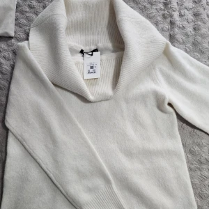 Vit stickad tröja med polokrage - Säljer en stilren vit stickad tröja med en bred polokrage. Tröjan har långa ärmar och är perfekt för kyligare dagar. Den är mjuk och bekväm, vilket gör den till ett måste i garderoben. Passar bra till både jeans och kjol. Off shoulder.