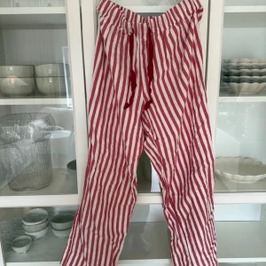 Randiga byxor från H&M - Säljer ett par randiga byxor från H&M i rött och vitt. Byxorna har en loose passform och är tillverkade i bomull. Perfekta för en avslappnad stil med elastisk midja och snörning. Jag har storlek 34 och dessa är jättesköna om man vill ha oversize pyjamasbyxor.