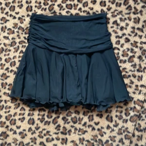 Svart kjol med volang - Snygg svart kjol med volangdetaljer. Kjolen har en kort längd och är perfekt för att ge en chic look. Den är tillverkad i ett lätt och flödande material som ger en fin rörelse.