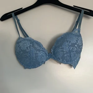 Blå spets-bh - Säljer en vacker blå bh med spetsdetaljer. Den har justerbara axelband och en fin blommig spetsdesign som ger en romantisk känsla. Perfekt för att känna sig extra fin under kläderna.