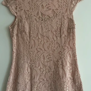 Rosa spetsklänning från Chiara Forthi - Elegant rosa spetsklänning från Chiara Forthi med korta ärmar och dragkedja i ryggen. Perfekt för en stilfull look med sitt vackra spetsmönster. Klänningen har en feminin och romantisk känsla.
