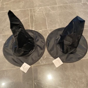 Svarta häxhattar från Hisab Joker - Två svarta häxhattar från Hisab Joker, perfekta för Halloween eller maskerad. Tillverkade i ett lätt och formbart material med en klassisk spetsig form och bred brätte.