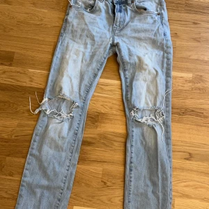 Ljusblå jeans med slitningar - Säljer ett par ljusblå jeans med coola slitningar på knäna. De har en klassisk femficksdesign och en bekväm passform. Perfekta för en avslappnad stil.