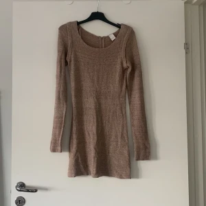 Beige stickad klänning från Vila - Snygg beige stickad klänning från Vila i storlek S. Klänningen har en rund halsringning och långa ärmar. Perfekt för kyligare dagar med sin mysiga stickade design. Den har en dragkedja i ryggen för enkel påklädning.