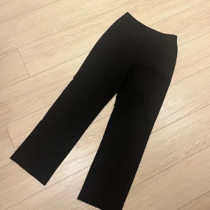 Svarta kostymbyxor från Vero Moda - Snygga svarta kostymbyxor från Vero Moda med en klassisk design. Byxorna har en rak passform och är perfekta för en stilren look. Tillverkade i ett bekvämt material som ger en elegant känsla.