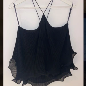 Svart plisserad linnetopp från Copenhagen Muse - Snygg svart plisserad linnetopp från Copenhagen Muse med tunna axelband och volangdetaljer. Perfekt för en stilren look med en touch av elegans. Axelbanden är justerbara för bästa passform.