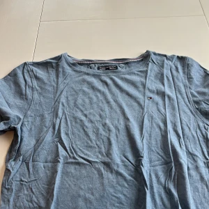Blå t-shirt från Tommy Hilfiger - Säljer en stilren blå t-shirt från Tommy Hilfiger. Den har en liten broderad logga på bröstet och är tillverkad i mjukt bomullsmaterial. Perfekt för en avslappnad look.