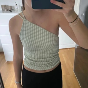 Grön- och vitrutad oneshoulder topp - Snygg grön- och vitrutad oneshoulder topp med smala axelband. Köpt på pull and bear, använd fåtal gånger så bra skick!