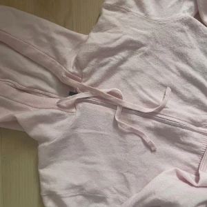 Rosa hoodie med dragkedja - Säljer en söt rosa hoodie med dragkedja och huva. Tröjan har långa ärmar och ribbade muddar vid ärmslut och nederkant. Perfekt för en avslappnad stil.