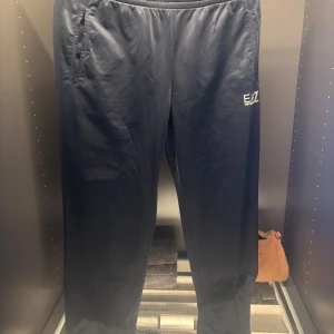 Svarta byxor från Emporio Armani - Snygga svarta byxor från Emporio Armani med elastisk midja och diskret logga på sidan. Perfekta för en avslappnad och stilren look. Byxorna har en enkel design med fickor på sidorna.