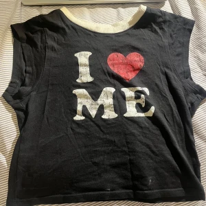 Svart kortärmad topp från H&M Divided - Säljer en svart kortärmad topp från H&M Divided med texten 'I ❤️ ME' i vitt och rött framtill. Toppen har en rund halsringning med vit kant och är perfekt för en avslappnad stil.  inga större skador utan de som visas i bilden. 