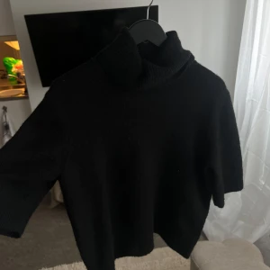 Svart polotröja - Säljer en stilren svart polotröja med trekvartsärm. Perfekt för kyligare dagar och enkel att matcha med olika outfits. Tröjan har en hög krage som ger extra värme och stil.