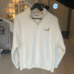 Vit tröja med dragkedja från Carhartt - Säljer en stilren vit tröja från Carhartt med halv dragkedja och broderad logga på bröstet. Perfekt för en avslappnad look. Tröjan har långa ärmar och en bekväm passform. Nypris 1199, säljs nu endast för 599. Tröjan är i toppskick! Personen på bilden är 175 cm lång o väger 80 kg. Skriv vid frågor!