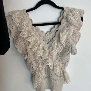 Beige spetsprydd topp från Zara - Säljer en elegant beige topp från Zara med vackra spetsdetaljer och volanger. Toppen har en v-ringad design och är perfekt för en stilfull look. 