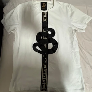 Vit t-shirt med svart orm från Glorious Gangsta - Säljer en vit t-shirt från Glorious Gangsta med en svart orm i skinn broderad på framsidan. Perfekt till sommaren.