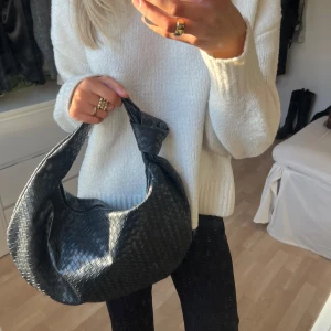 Svart flätad axelväska - Snygg svart axelväska med flätat mönster och knutdetalj på handtaget. Väskan har en dragkedja för säker förvaring av dina saker. Väldigt rymlig och stilren! 💓 inga defekter! Perfekt till typ skolan eller när man går ut. Den är 45,7cm bred och 25,4cm hög