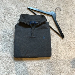 Ralph Lauren Quarter Zip  - Säljer en stilren grå tröja från Ralph Lauren med dragkedja vid halsen. Tröjan har långa ärmar och är perfekt för en avslappnad look. Den är tillverkad i ett mjukt material som ger en bekväm passform. Själva dragkedjan är borta men går att dra upp och ner, som visas på bild 4. Nytt pris 2000kr+!!!