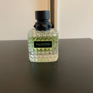 Valentino parfym  - Snygg parfymflaska från Valentino med en unik design. Flaskan är genomskinlig med ett grönt skimmer och har en svart kork med nitar. Perfekt för den som vill ha en stilren och modern look på sin parfymhylla. Köpte utan att ha luktat på doften, oanvänd men hittar inte boxen. 50ml.