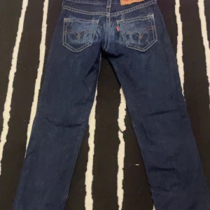 Blå jeans från Levi's - Säljer ett par klassiska blå jeans från Levi's med snygga kontrastsömmar och femficksdesign. De har en normal passform och är perfekta för en avslappnad stil. Levi's logotyp syns tydligt på bakfickan. Waist 26. 