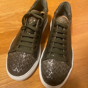  Oanvända sneakers i kalvskinn mörkgröna - Snygga handgjorda mörkgröna sneakers i kalvskinn med matchande snörning. Skorna har en vit sula som ger en fräsch kontrast. Perfekta för en stilren look. Skorna är handgjorda i Italien och köpta på CC Shoes i Sturegallerian. Ordinarie pris är 4500kr. Storlek 40 1/2, men passar även 41. 