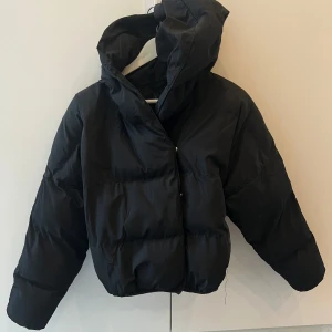 Svart dunjacka med huva - Pufferdesign med 2 rader knappar framtill. (En rad i mitten och en lite mer åt höger som bilden visar)🥰 En aning sliten. inte helt säker att den är från Zara då jag inte är hemma när jag laddar upp den här, men kan dubbelkolla det om det skulle vara viktigt! 