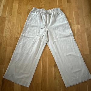 Beige linnebyxor med resårmidja - Snygga beige linnebyxor med loose passform och hög midja. Byxorna har en bekväm resårmidja med snörning för justerbar passform. Perfekta för en avslappnad stil. Aldrig använda 