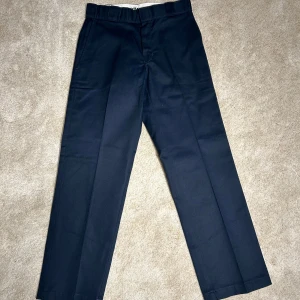 Dickies - Snygga marin blåa byxor från Dickies, modell 874 med original passform. Byxorna har en klassisk design med dragkedja och knapp framtill. Perfekta för en stilren look.