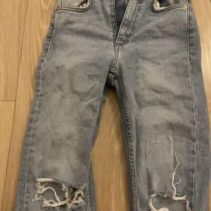 Säljer ett blå grå jeans med coola slitningar på knäna. De har en klassisk femficksdesign och dragkedja. Perfekta för en avslappnad stil.