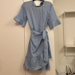 Ljusblå klänning från Vero Moda - Säljer en jättefin ljusblå klänning som är perfekt till vår/sommar från Vero Moda med knytband i midjan och volanger. Jag har använt den max 2 gånger och jag säljer den på grund av att den inte kommer till användning. Skriv till mig om de är något mer du vill veta eller har intresse för att köpa. 