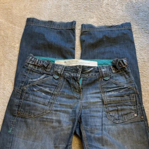 Blå jeans med detaljer - Snygga blå jeans med coola detaljer som knappar och dragkedja. De har en klassisk femficksdesign och en unik söm längs fickorna. Perfekta för en avslappnad stil.