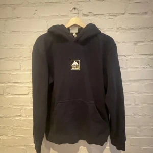 Svart hoodie från H&M - Säljer en svart hoodie från H&M med tryck av 'Nation Nature' på bröstet och ryggen. Tröjan har en klassisk känguruficka och en bekväm huva. Perfekt för en avslappnad stil.