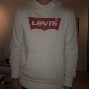 Vit hoodie från Levi's - Säljer en vit hoodie från Levi's med röd logga på bröstet. Tröjan är i jätte bra skick nästan helt ny! Endast testad! Tröjan är i Stl 164. 