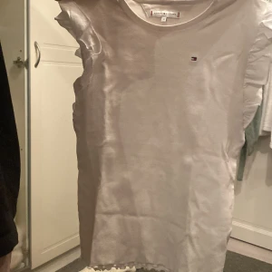 Vit ribbad t-shirt från Tommy Hilfiger - Säljer en vit ribbad t-shirt från Tommy Hilfiger med korta ärmar och liten logga på bröstet. Perfekt för en avslappnad stil. T-shirten har en rund halsringning och är i ett mjukt material.