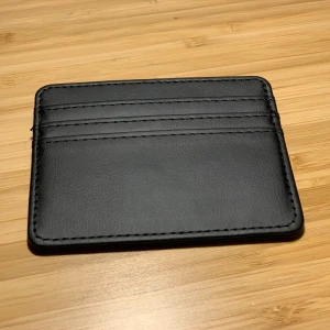 Svart plånbok  - Säljer en stilren och praktisk svart plånbok i skinn. Den har flera kortfack och är perfekt för att hålla dina kort organiserade. Plånboken är i mycket bra skick och passar perfekt i fickan. Perfekt för vardagsbruk eller när du vill resa lätt.