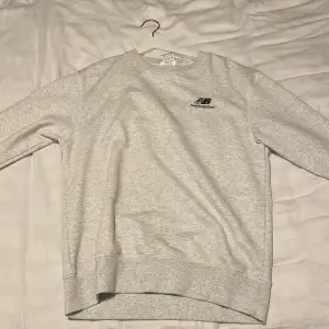 Säljer en stilren grå sweatshirt från New Balance i mycket bra skick. Den har en klassisk rund hals och långa ärmar, perfekt för både vardag och träning. Materialet är mjukt och bekvämt, vilket gör den idealisk för höst och vår. Enkelt New Balance-märke på bröstet.