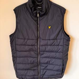 Säljer en svart quiltad väst från Lyle & Scott i storlek 15/16 år. Västen har en dragkedja framtill och en broderad logga på bröstet. Perfekt för höst och vår, och den är både stilren och bekväm.