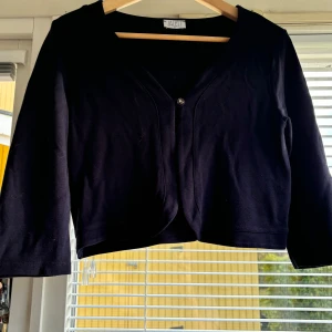 Svart kofta från Jacett - Säljer en stilren svart kofta från Jacett i storlek S. Koftan har trekvartsärmar och en enkel knapp framtill. Perfekt för både vardag och festliga tillfällen. Materialet känns mjukt och bekvämt. Passar bra till höst- och vintergarderoben!