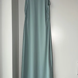 Ljusblå långklänning - Elegant ljusblå långklänning i ett mjukt och följsamt material. Klänningen har en tight passform som framhäver figuren och är perfekt för festliga tillfälle. Den är oanvänd 
