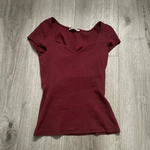 Vinröd ribbad topp från Anna Field - Säljer en snygg vinröd ribbad topp från Anna Field. Den har en v-ringad design och korta ärmar, perfekt för både vardag och fest. Toppen är i bra skick och har en tight passform som framhäver figuren. Perfekt för höst och vår!